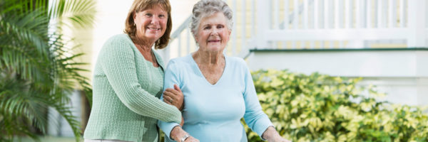 A woman helping another woman walk on sidewalk