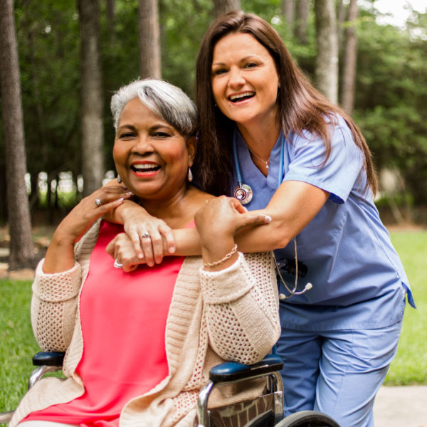 Elderly lady in wheelchair being hugged by nurse